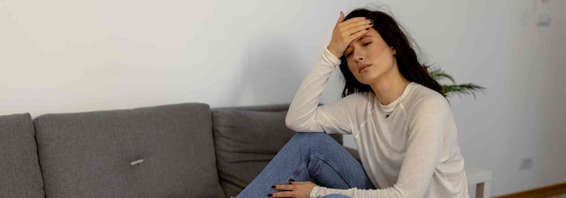 woman sitting on sofa holding her forehead in discomfort