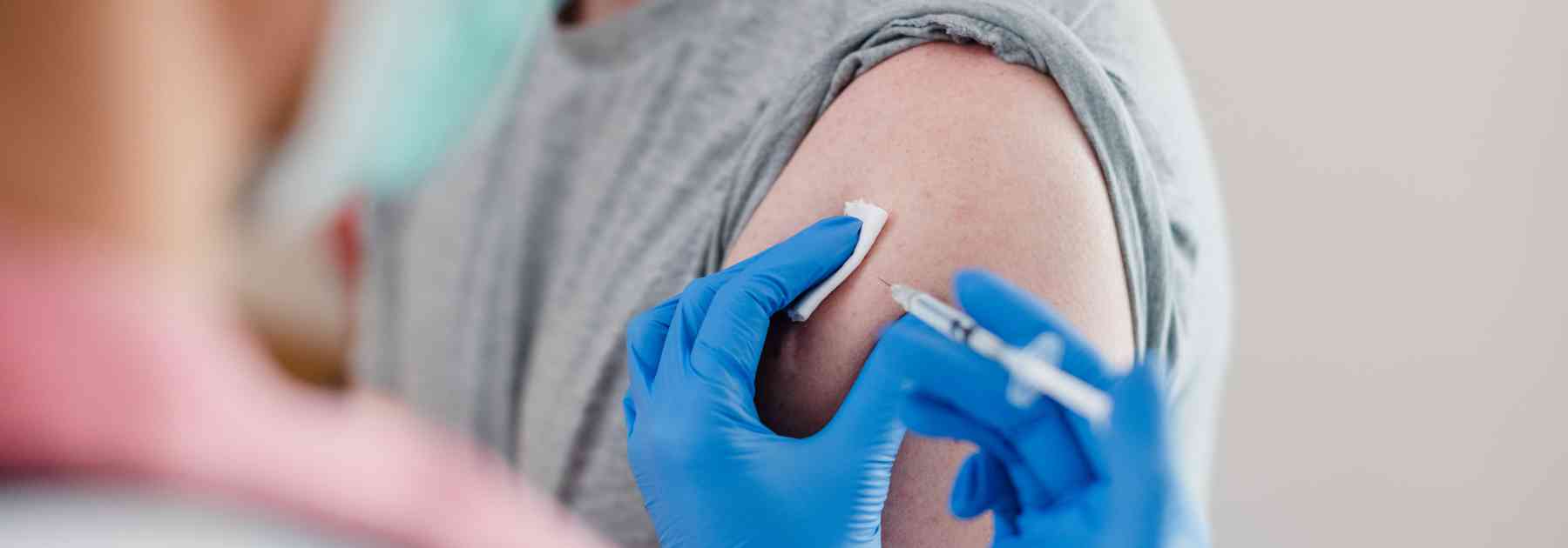male patient in grey shirt receiving vaccine in arm